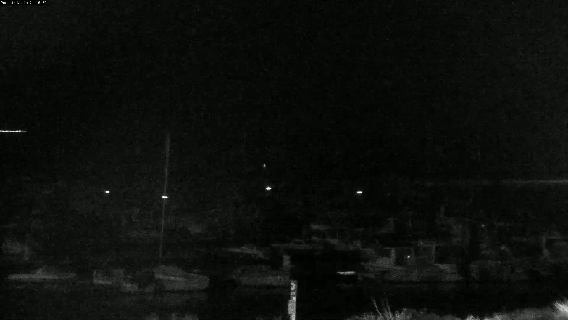 A nighttime, low-light view of a dark, possibly harbor area with faintly visible structures and a few distant lights.