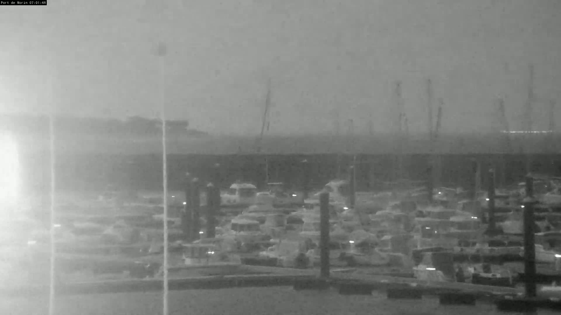 A hazy, low-light nighttime view shows many boats docked at a marina.