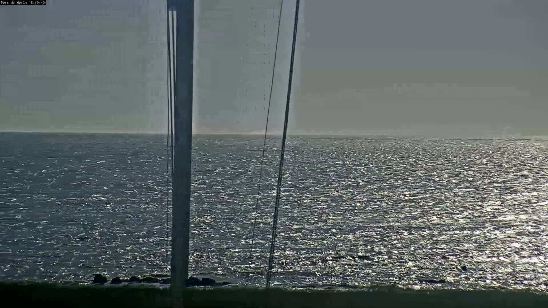 A mostly cloudy day shows a view of a moderately wavy ocean, partially obscured by what appears to be a tall mast or similar structure.