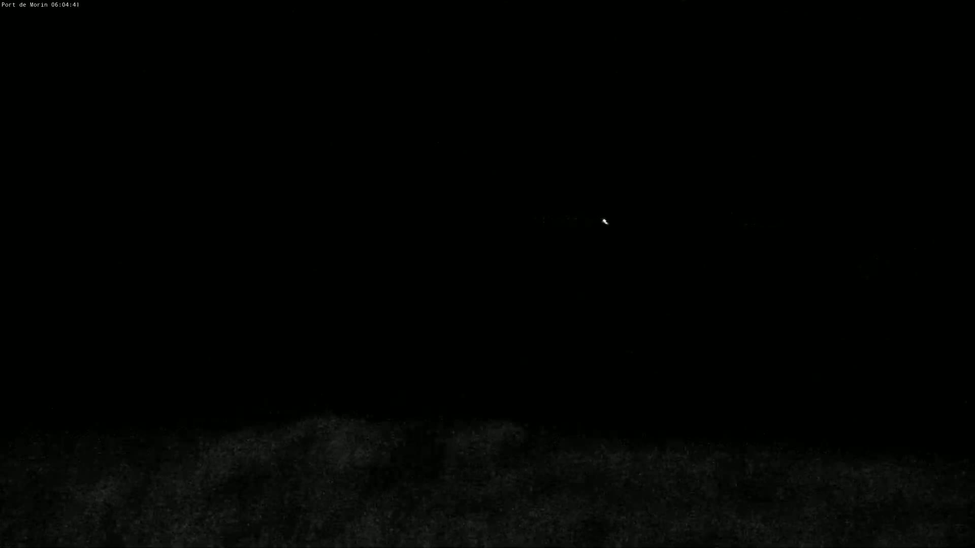 A dark, nighttime scene shows a faint light in the distance above a dark, textured ground.