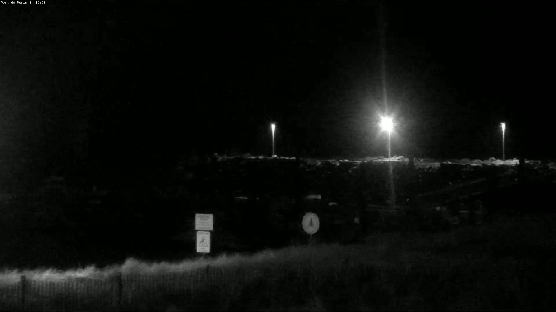 A nighttime, brightly lit parking lot is visible beyond a grassy area and fence.