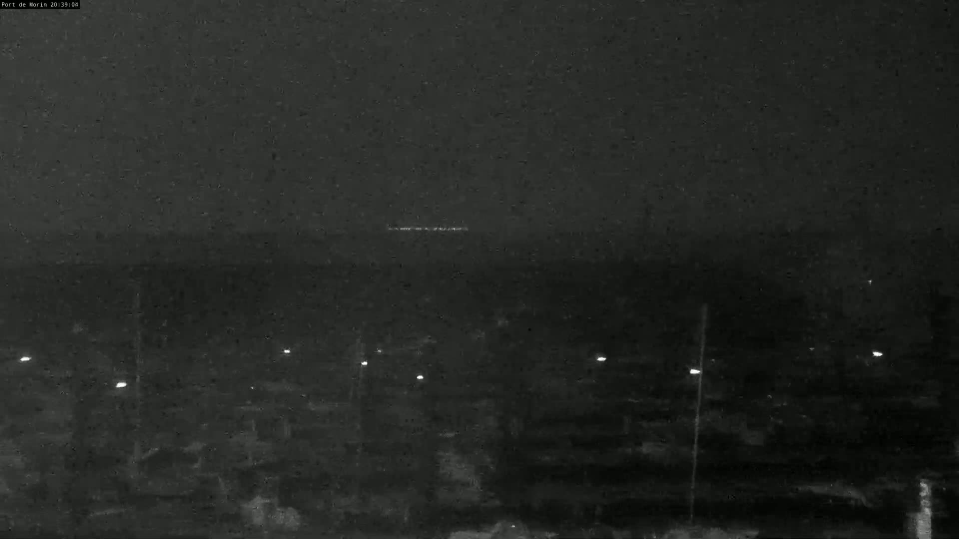 A nighttime, low-light image shows a dark landscape with a few distant lights and several closer, faint lights possibly from street lamps.