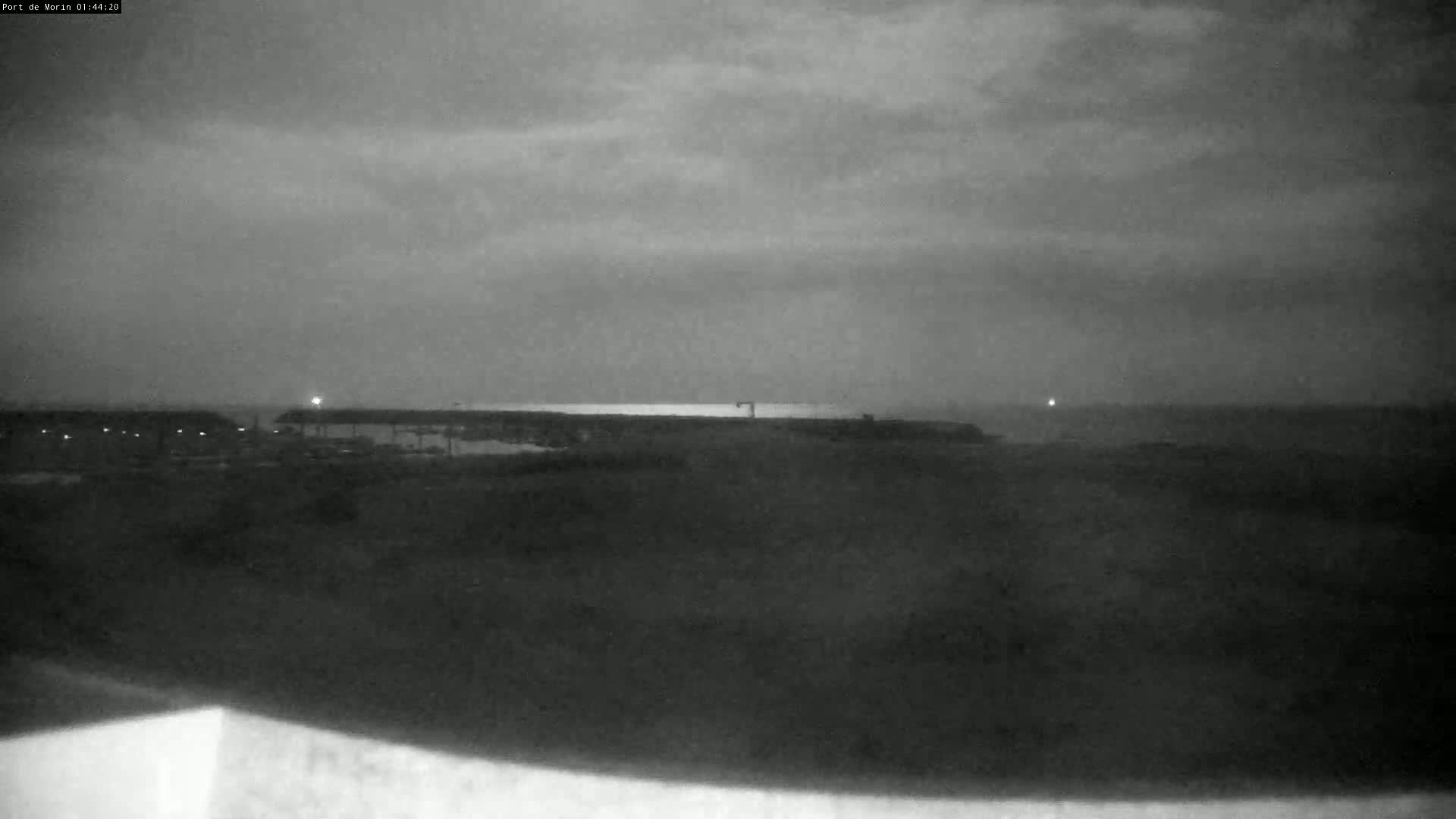 A nighttime, overcast view shows a flat, dark landscape with a faint light source in the distance.