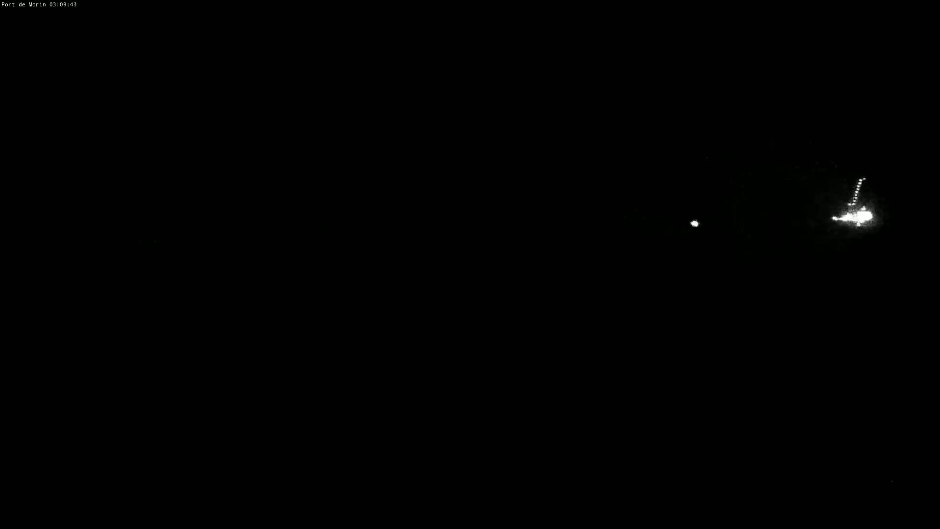 A nighttime image shows a few distant lights, possibly from vehicles or buildings, in an otherwise dark environment.