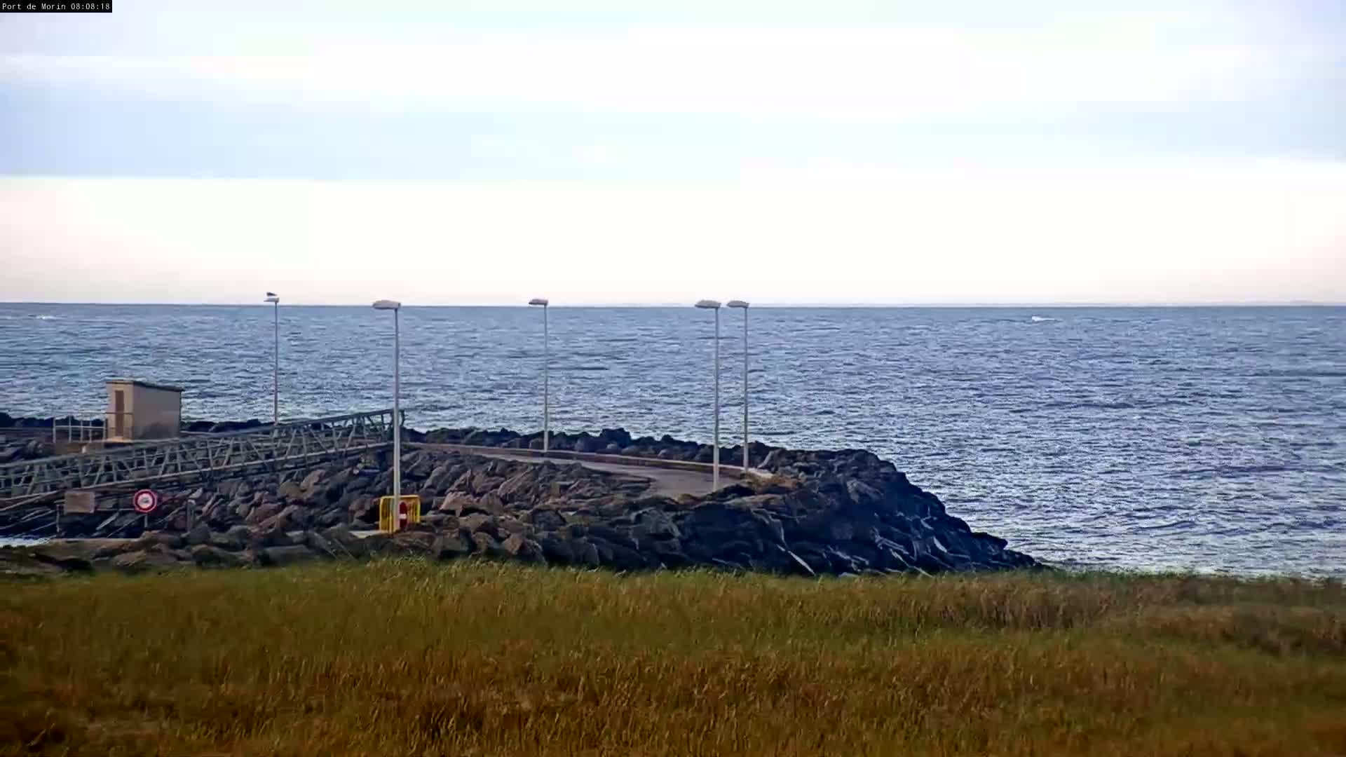 A rocky shoreline with a small pier and a calm sea under a mostly cloudy sky.
