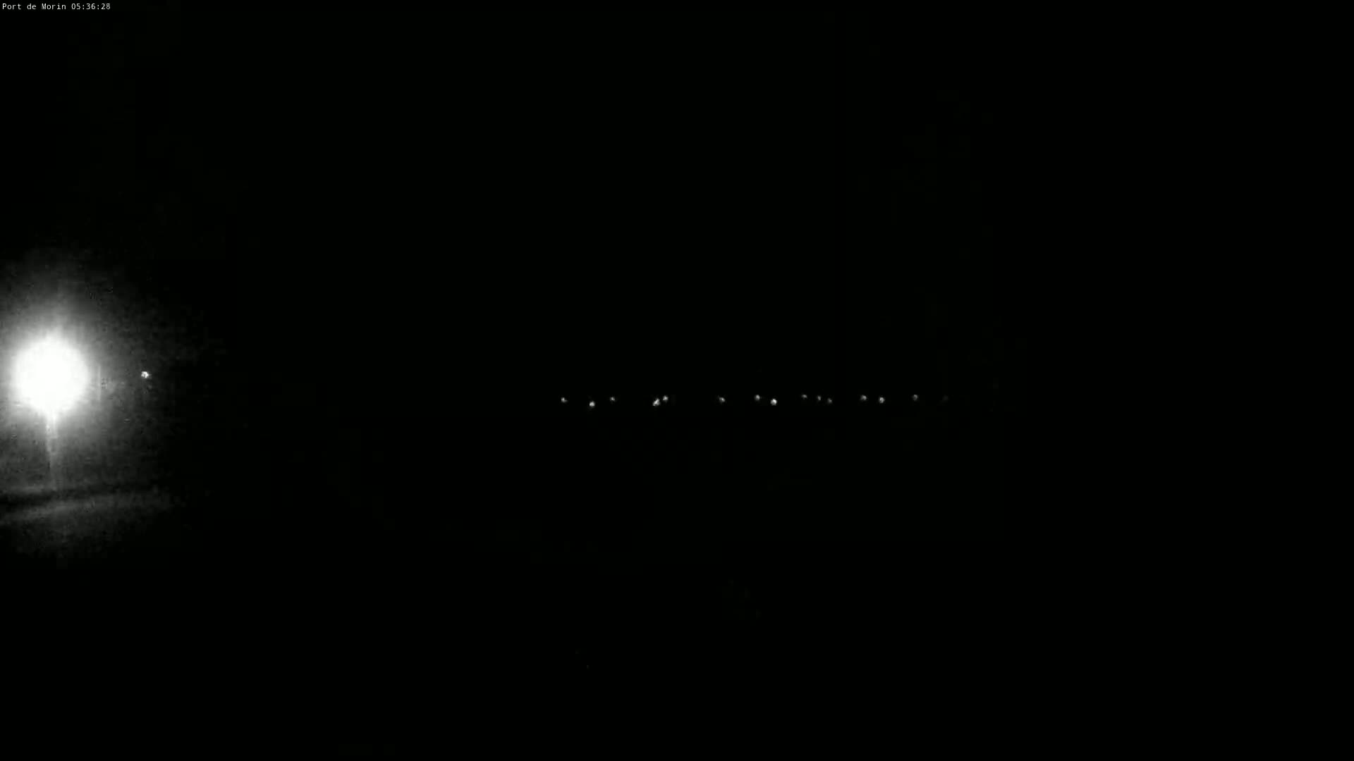 A bright light illuminates the left side of a dark, nighttime scene featuring a faint line of distant lights.