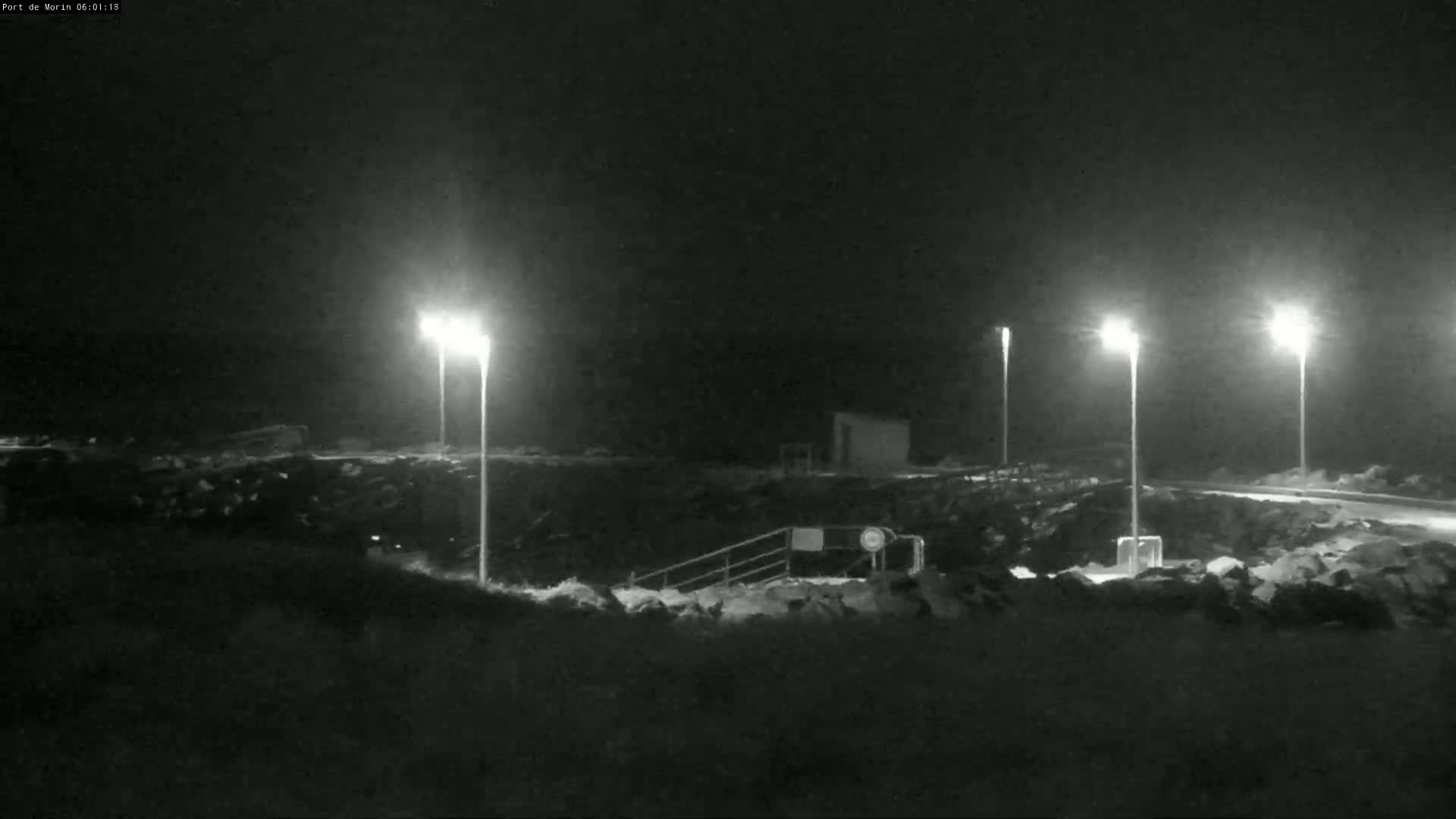 At night, under a dark sky, several bright lights illuminate a rocky area with a stairway leading down to a small structure.
