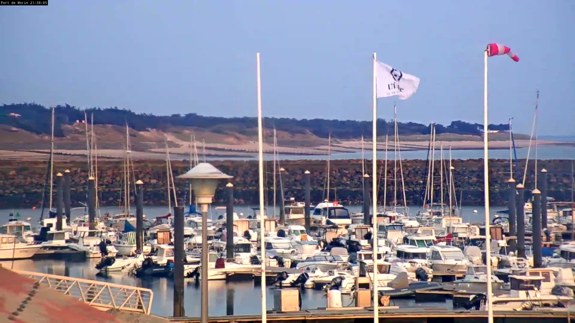 A marina filled with numerous boats under a clear sky, with a windsock indicating wind.