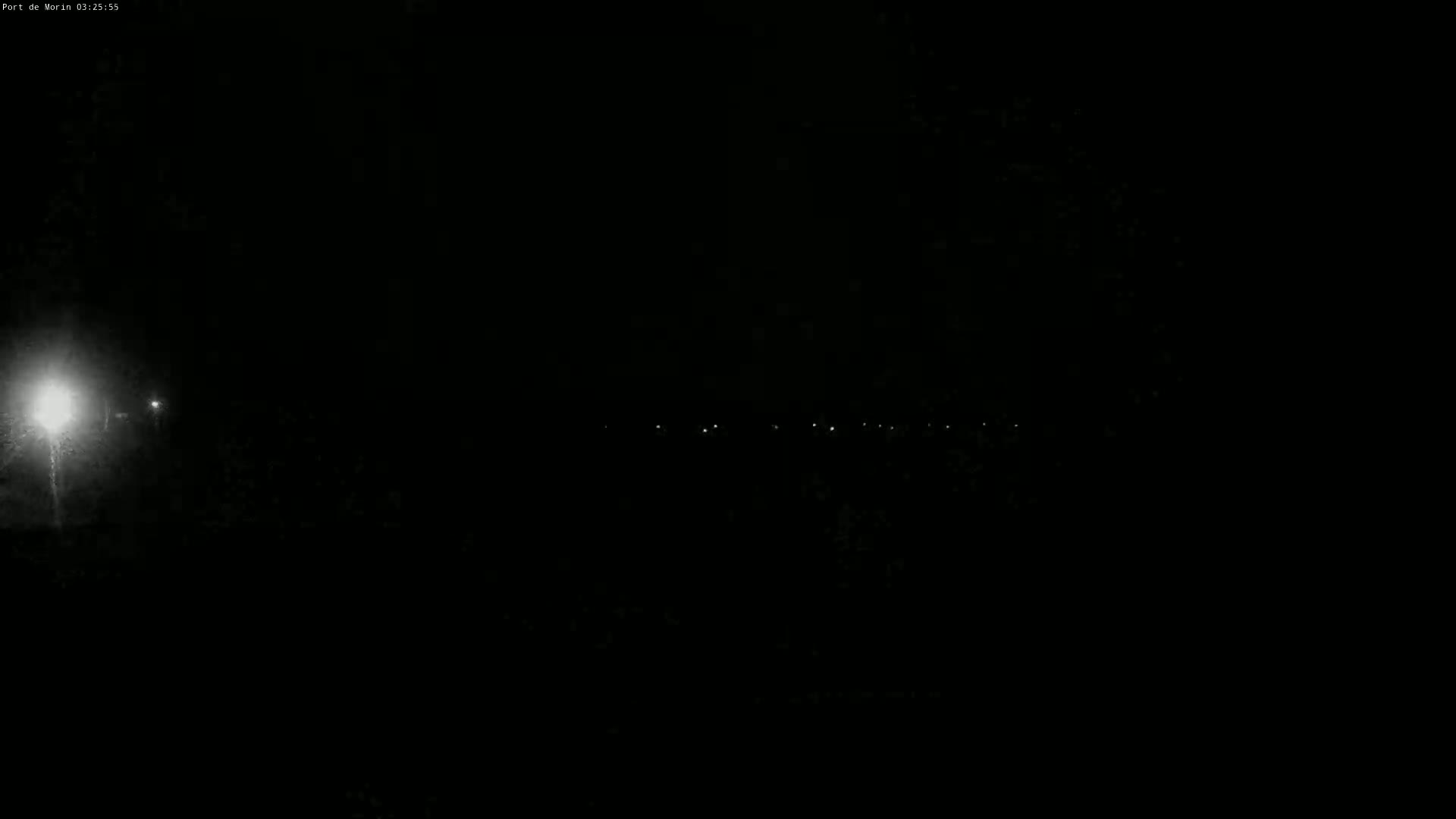 A nighttime, dark scene shows a few distant lights on the horizon, with one brighter light closer to the viewer in the left corner.
