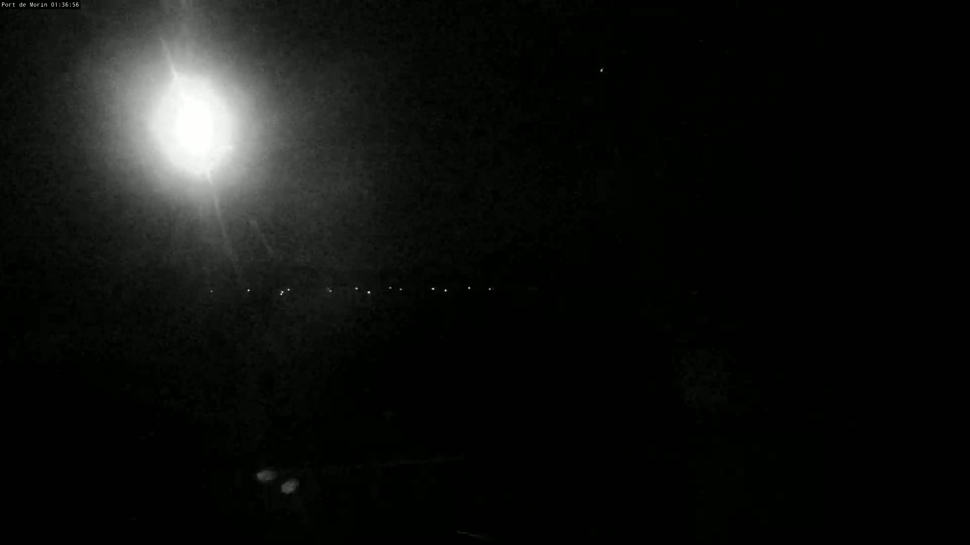 A bright light illuminates a dark, nighttime scene with a few faint lights visible in the distance.