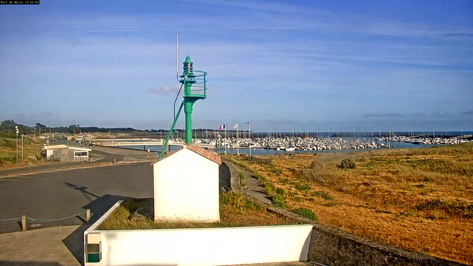 A green day marker stands near a harbor filled with numerous boats under a clear blue sky.