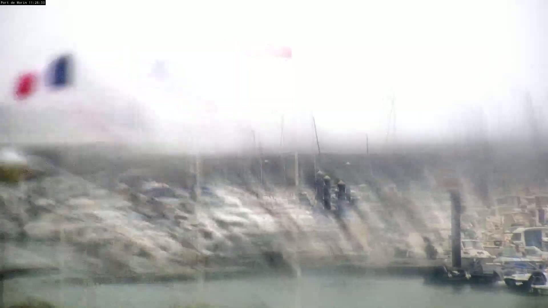 A blurry view of a harbor filled with boats in heavy rain and fog.
