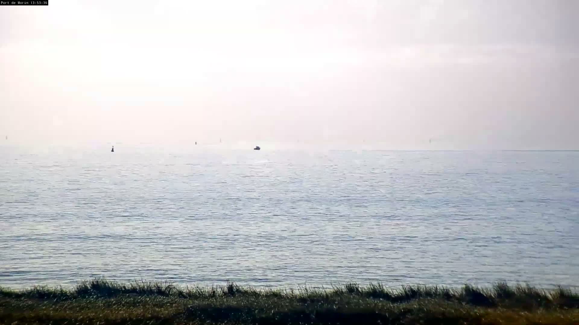 A nighttime, low-light image shows a bright light source in the sky above a dark landscape with distant lights and a body of water in the background.