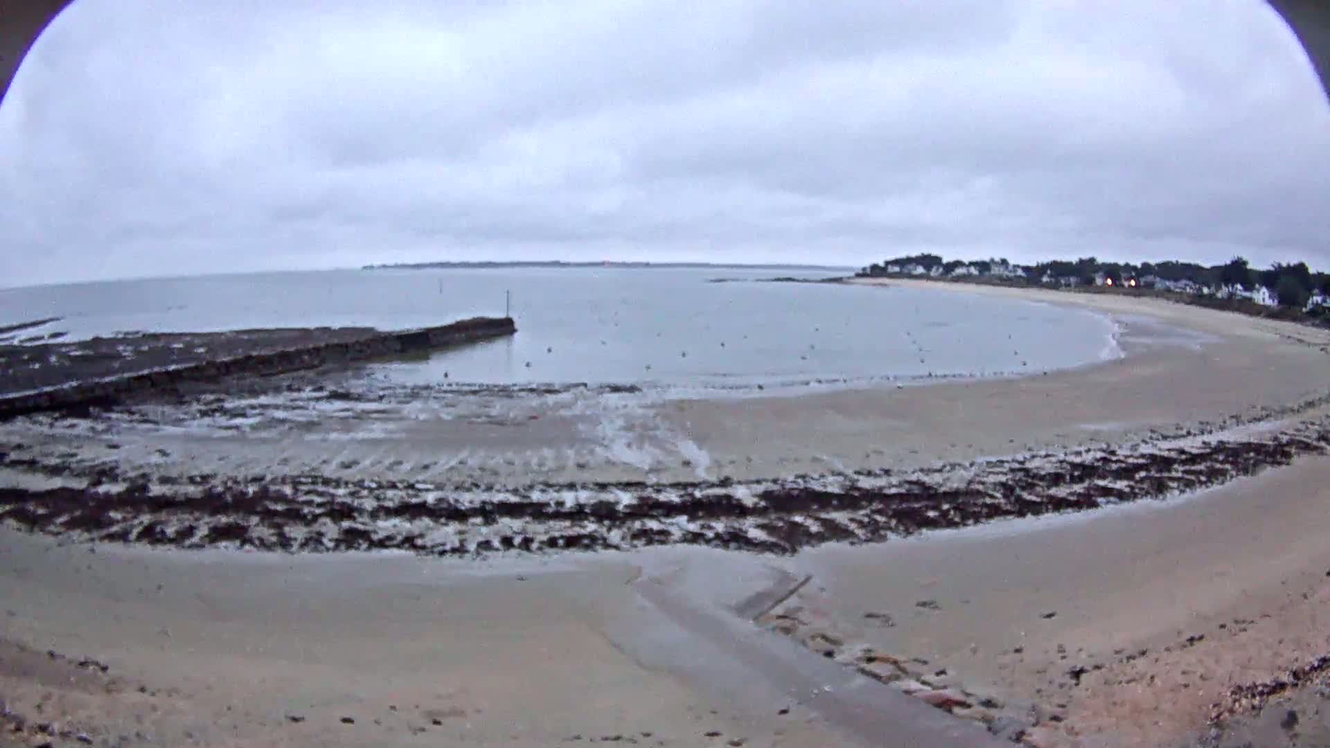 A sandy beach curves around a calm bay under an overcast sky.