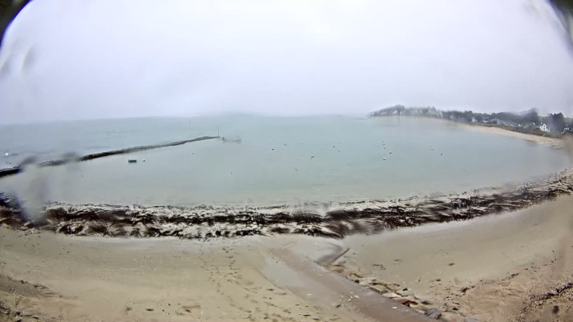 A sandy beach and calm bay are visible on an overcast day with rain.