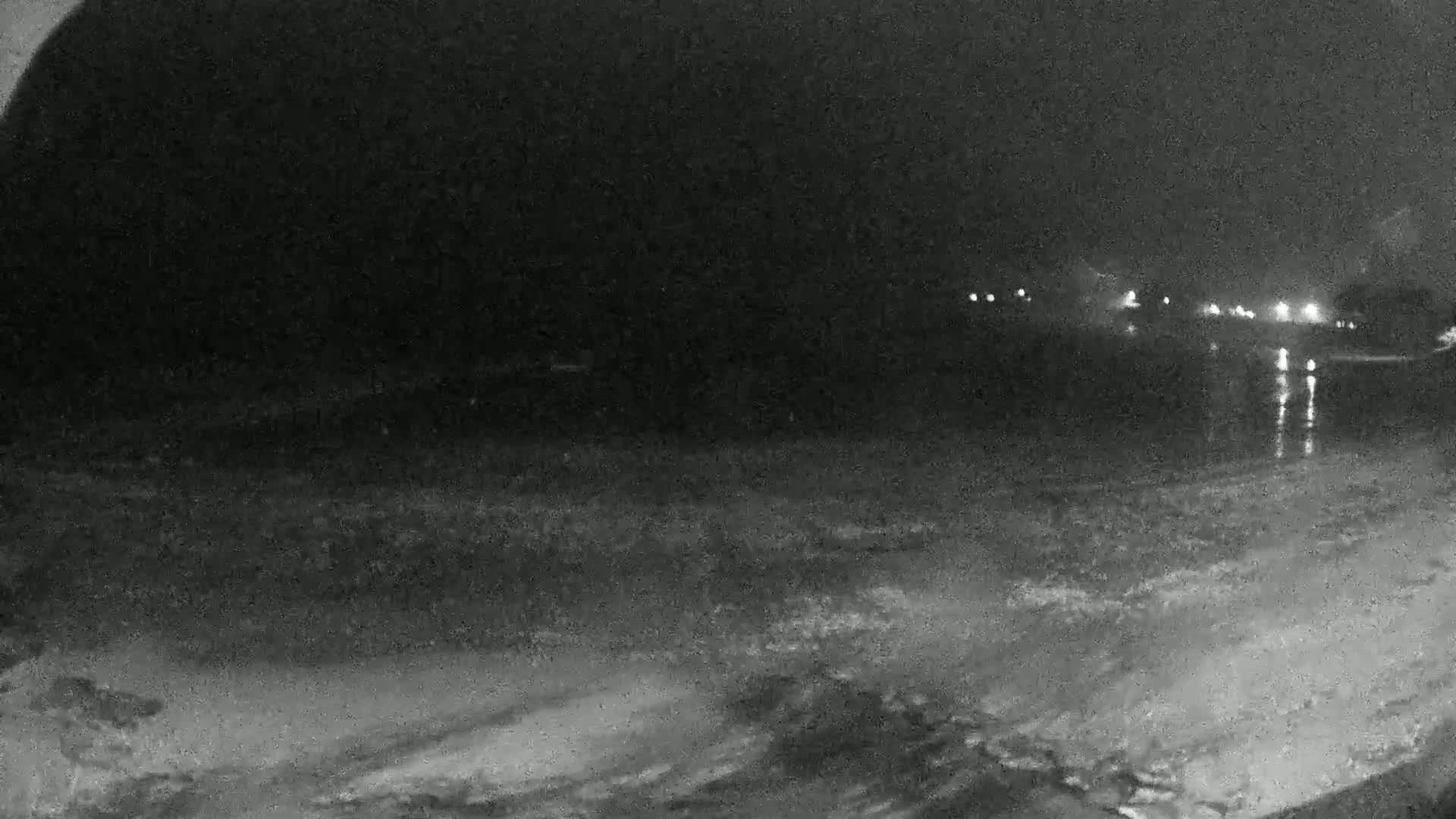 A nighttime view of a dark, still body of water with lights faintly visible in the distance across the water.