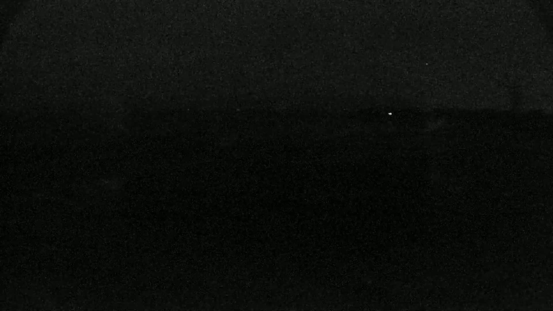 A dark, grainy image shows a mostly black expanse with a few very faint, tiny white specks.