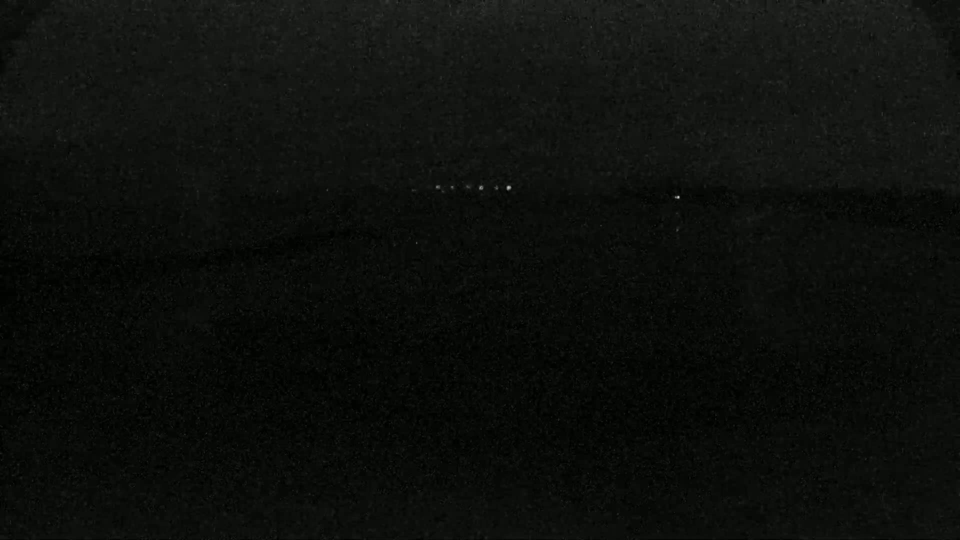 A dark, possibly nighttime, image shows a blurry line of faint lights on the horizon.
