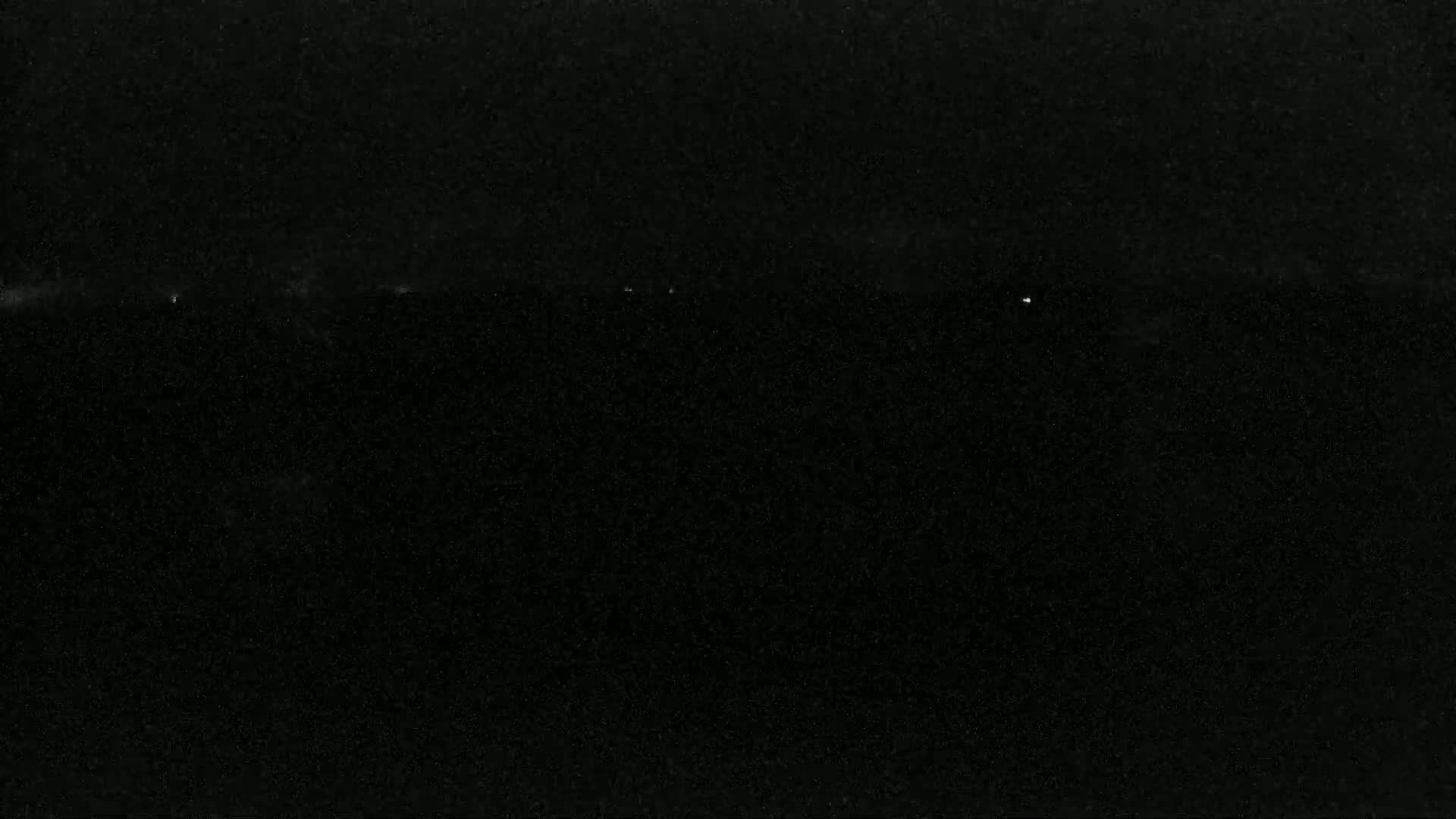 A nighttime, dark image shows a faint, horizontal band of light near the top and a few faint specks of light scattered across the bottom.