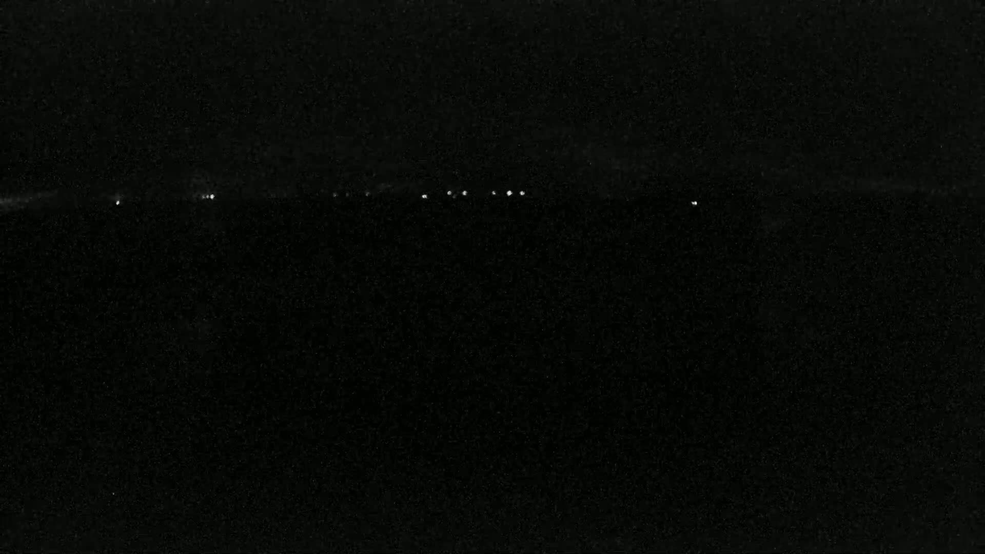A dark, possibly nighttime, scene shows a low horizon line with a few small, distant lights.