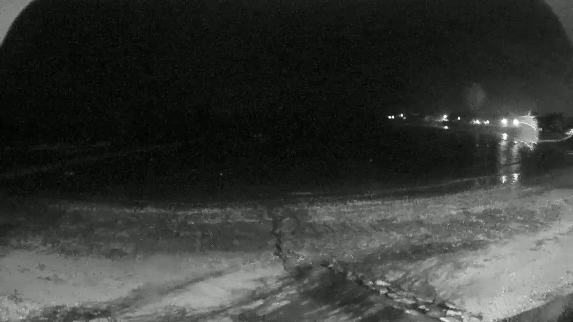 A nighttime, low-light view shows a dark beach with a dark body of water reflecting distant lights.