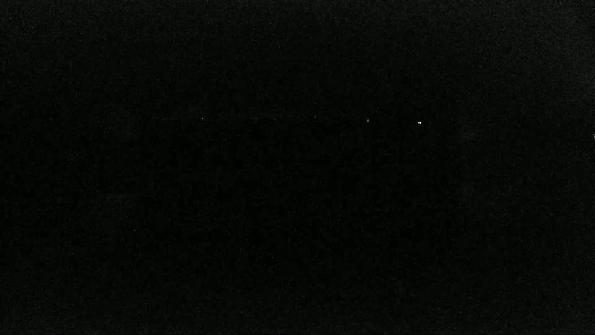 The image is a mostly black, grainy surface with a few specks of lighter gray.