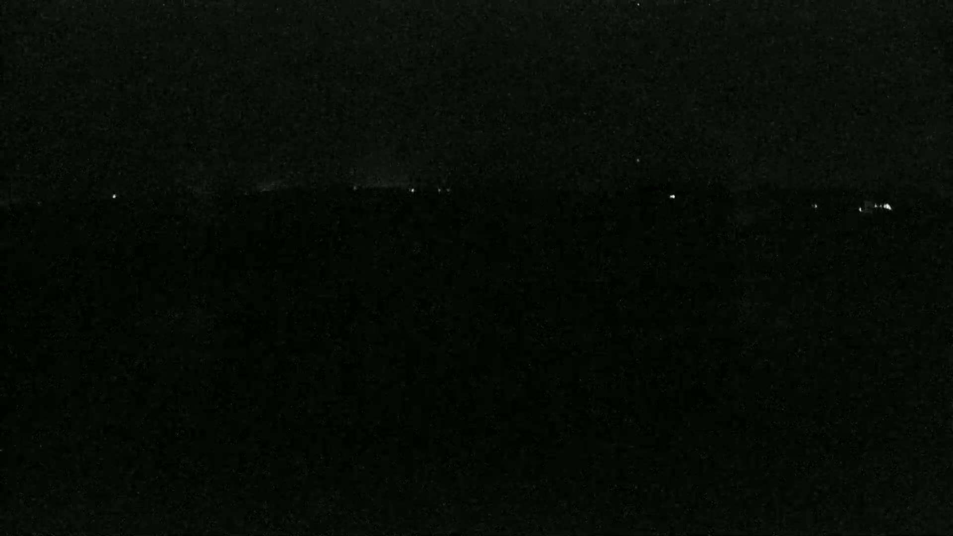 A nighttime, dark landscape is visible with a few faint lights on the horizon.