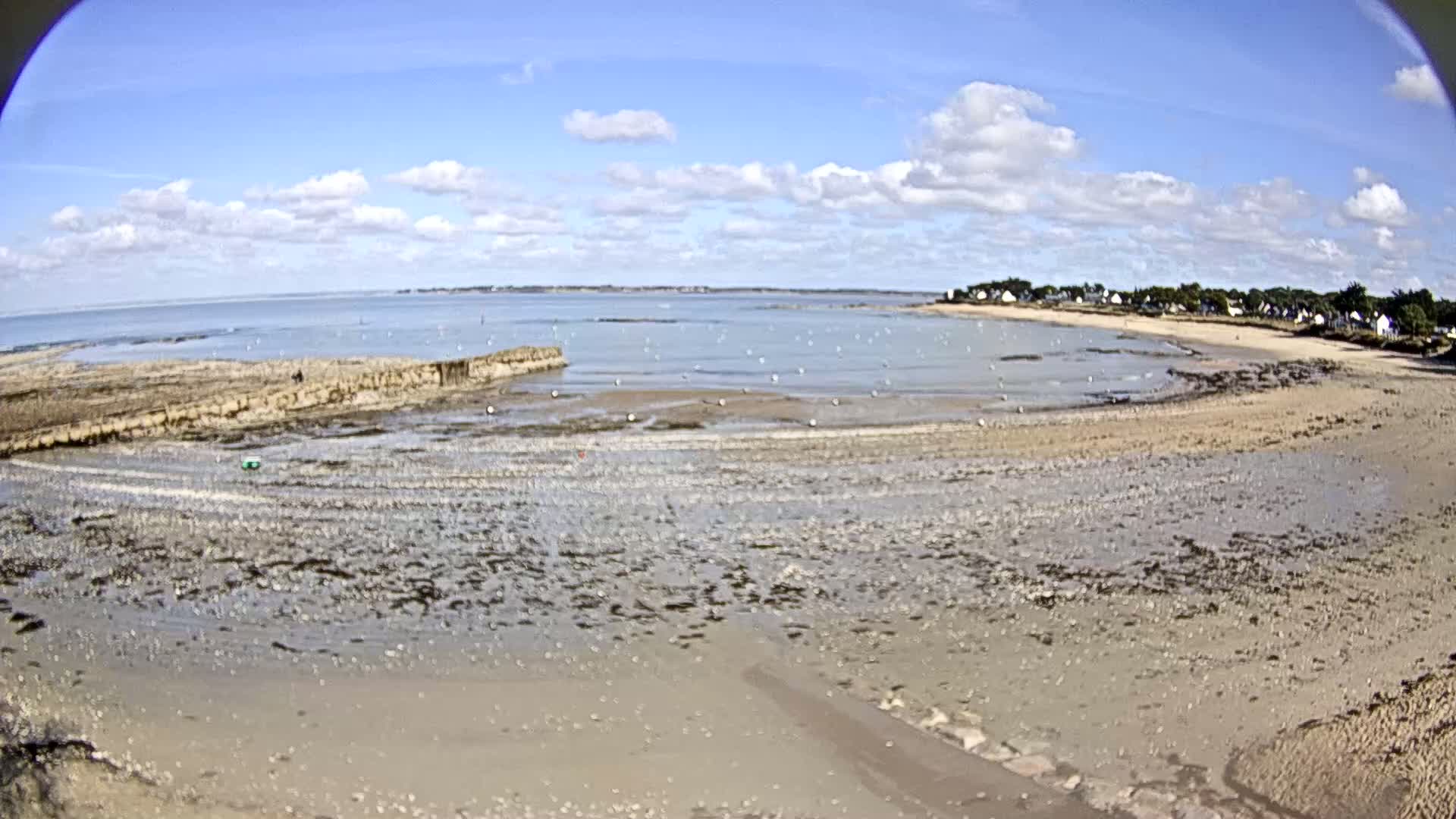 A wide sandy beach stretches out to a calm sea under a partly cloudy sky.