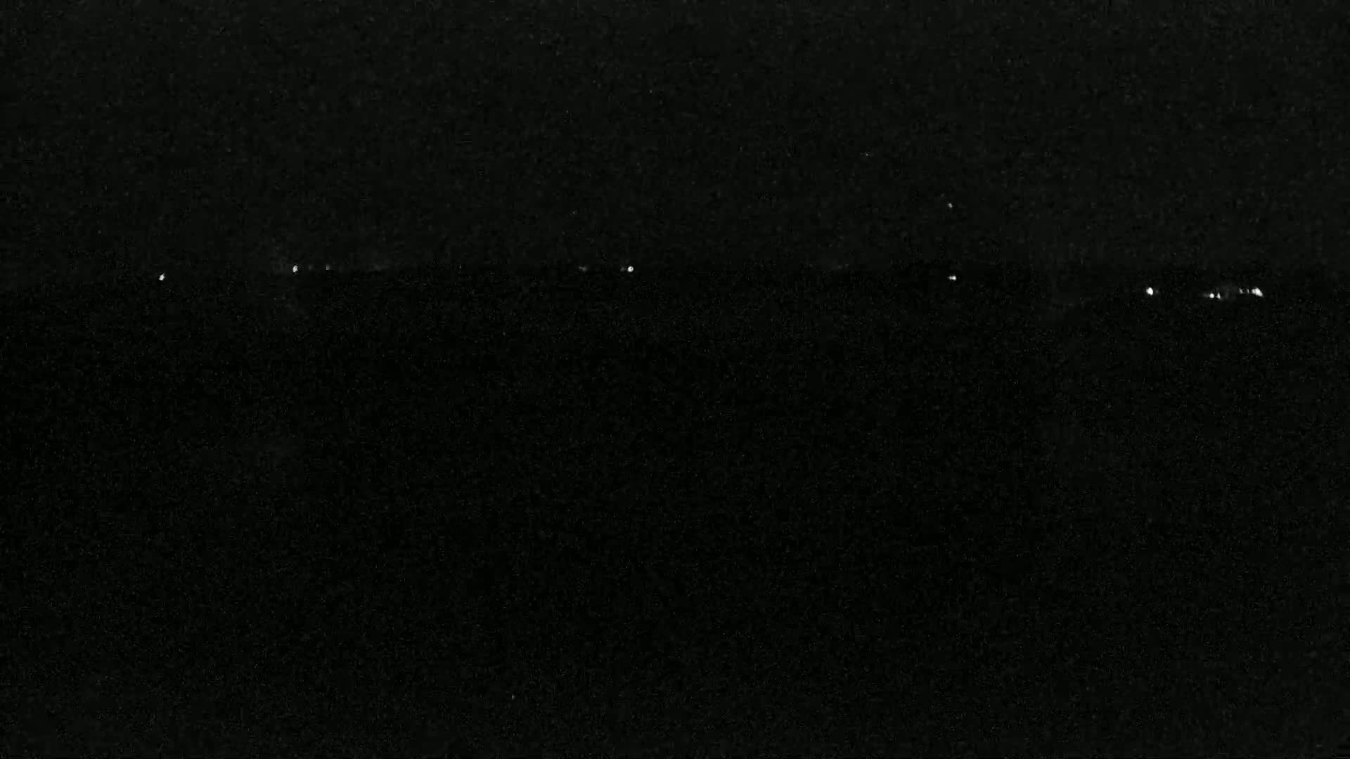 A dark, possibly nighttime, scene shows a few distant lights on a dark horizon.