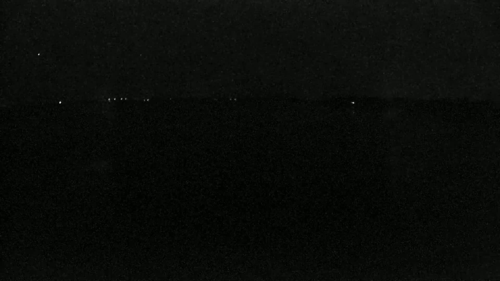 A dark, possibly nighttime, scene shows a few faint lights on the horizon.