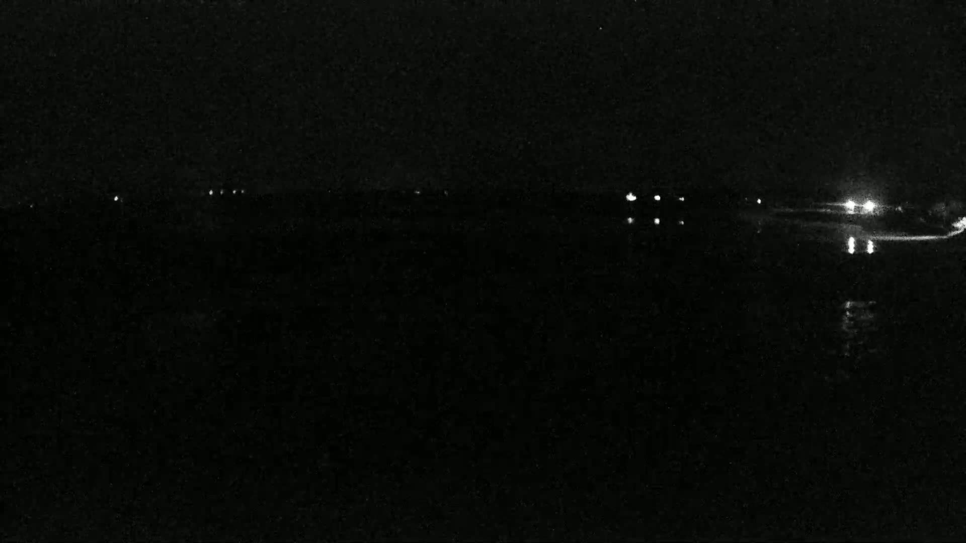 A dark, nighttime scene shows a body of water reflecting distant lights.