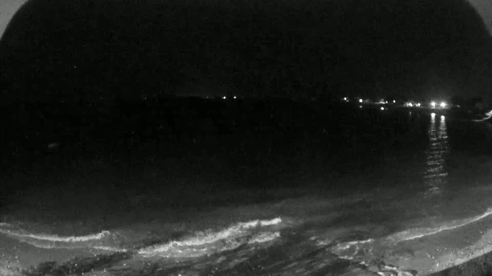 A dark nighttime beach scene shows gently lapping waves and distant lights across the water.