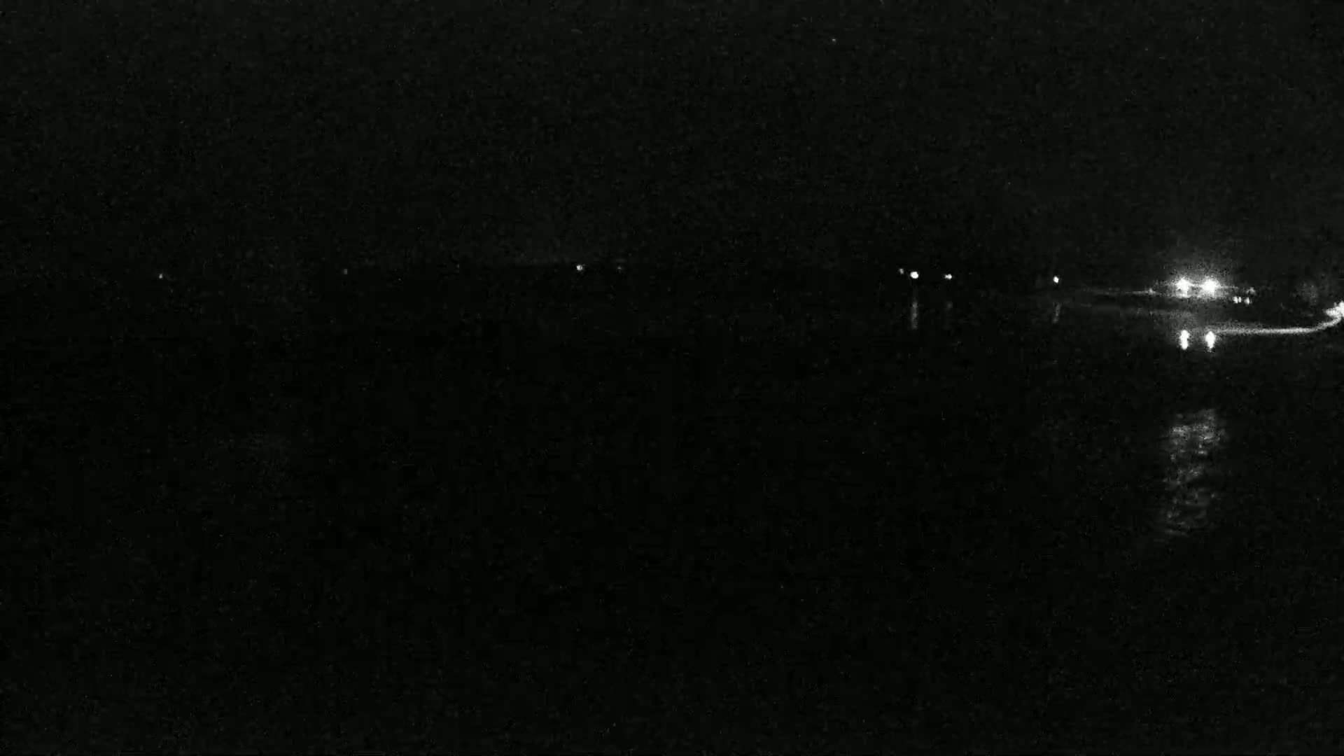 A nighttime, low-light view shows a dark landscape with a few faint lights in the distance.