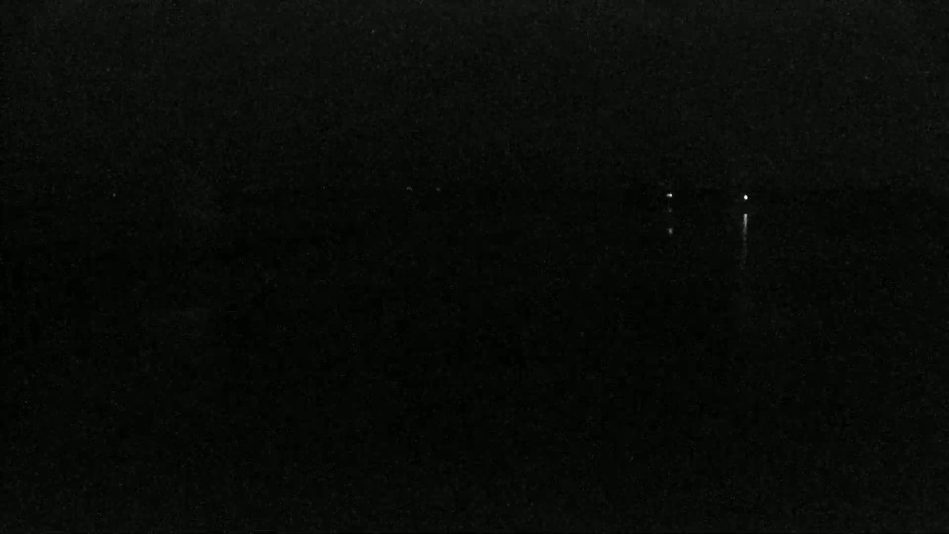 A dark, nighttime scene shows a body of water with a few faint lights visible in the distance.