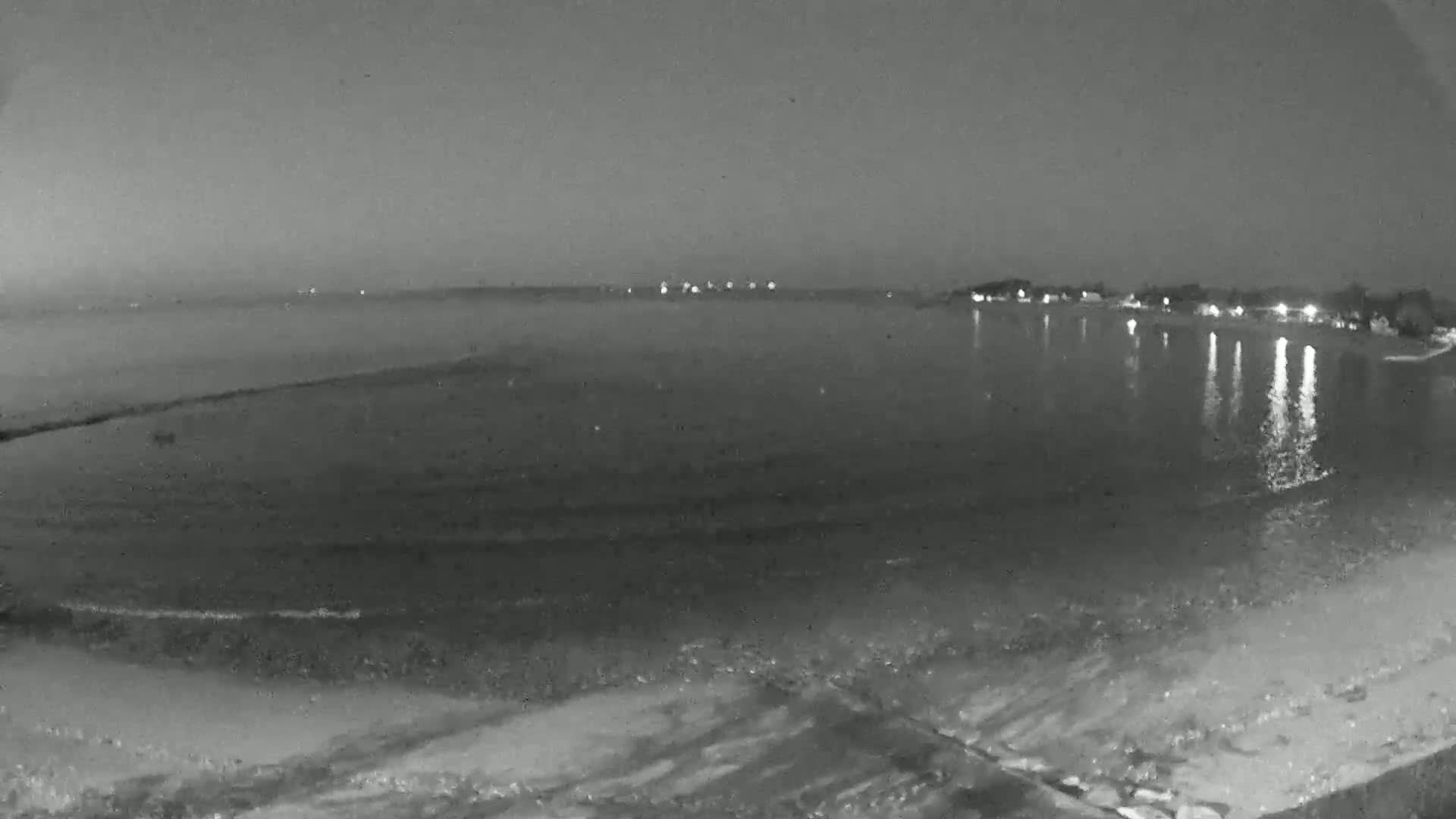 A nighttime view of a calm body of water with a shoreline showing some lights from buildings in the distance under a dark sky.