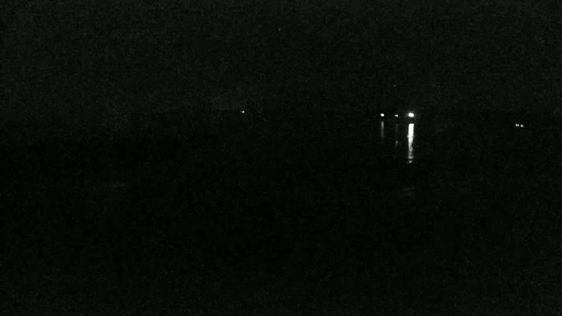 A dark, nighttime scene shows a few distant lights reflected on a dark body of water.