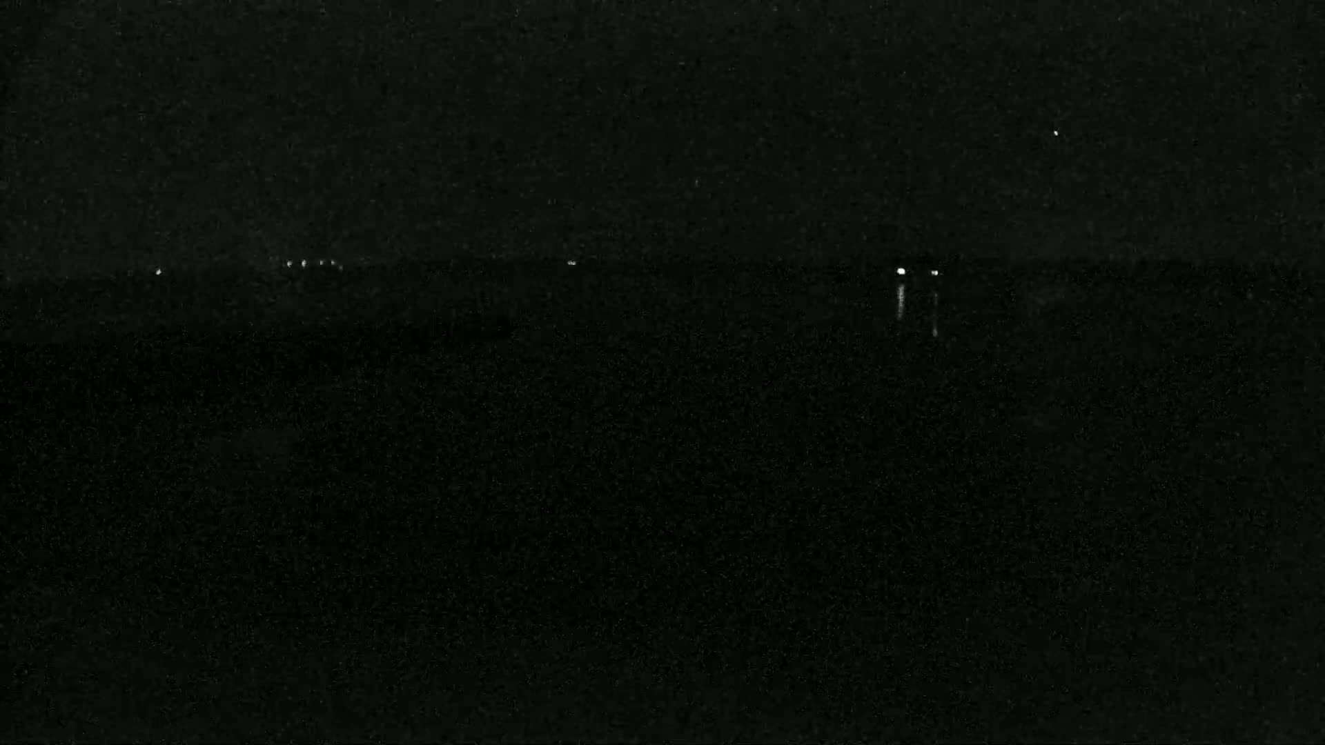 A dark, nighttime scene shows a faint horizon line with a few small, distant lights.
