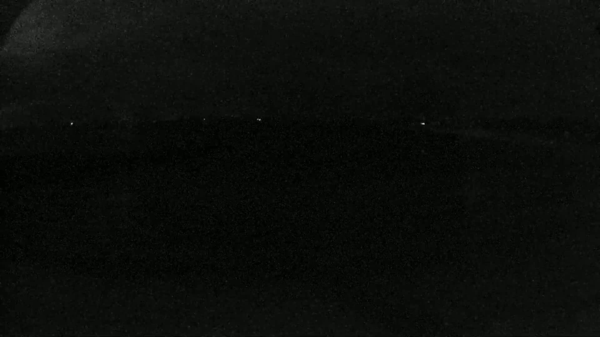 A mostly black image shows a dark, possibly nighttime, scene with a few faint, distant lights.