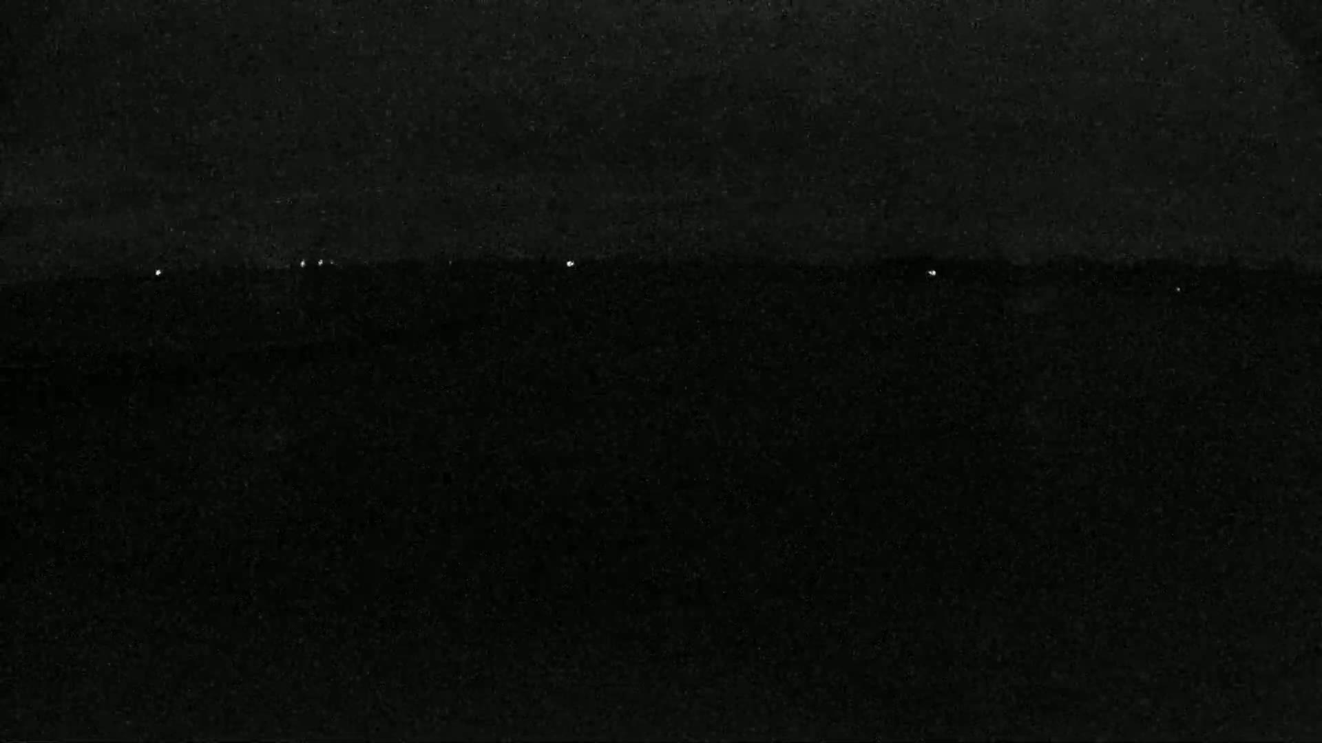 A nighttime image shows a dark, possibly grainy, surface with a few small, faint lights visible near the horizon.
