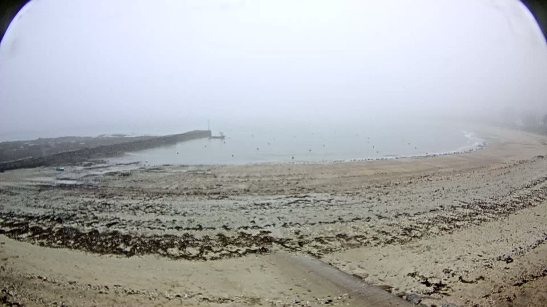 A foggy view of a sandy beach with a rocky breakwater and calm water in the background.