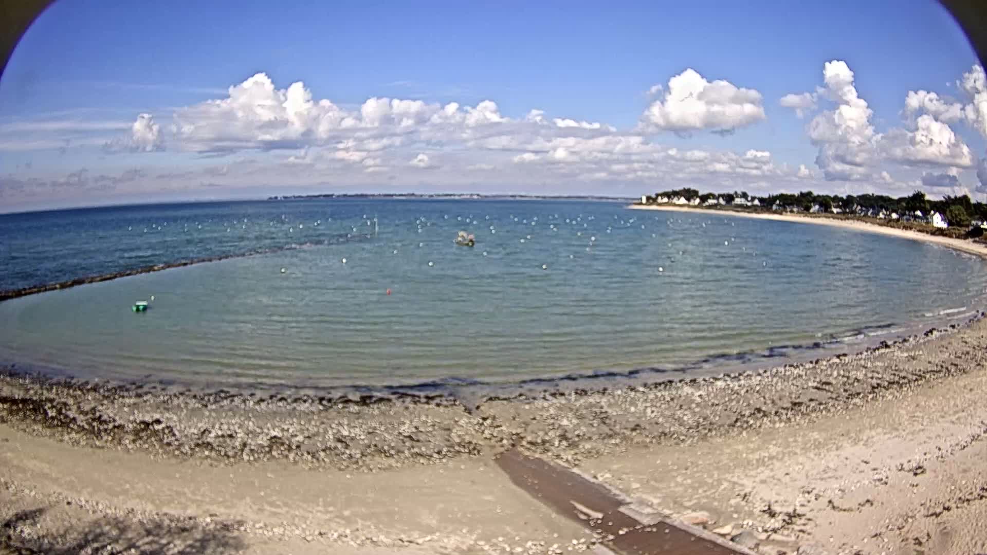 A partly cloudy sky overlooks a calm bay with a sandy beach and a small rocky area at the water's edge.