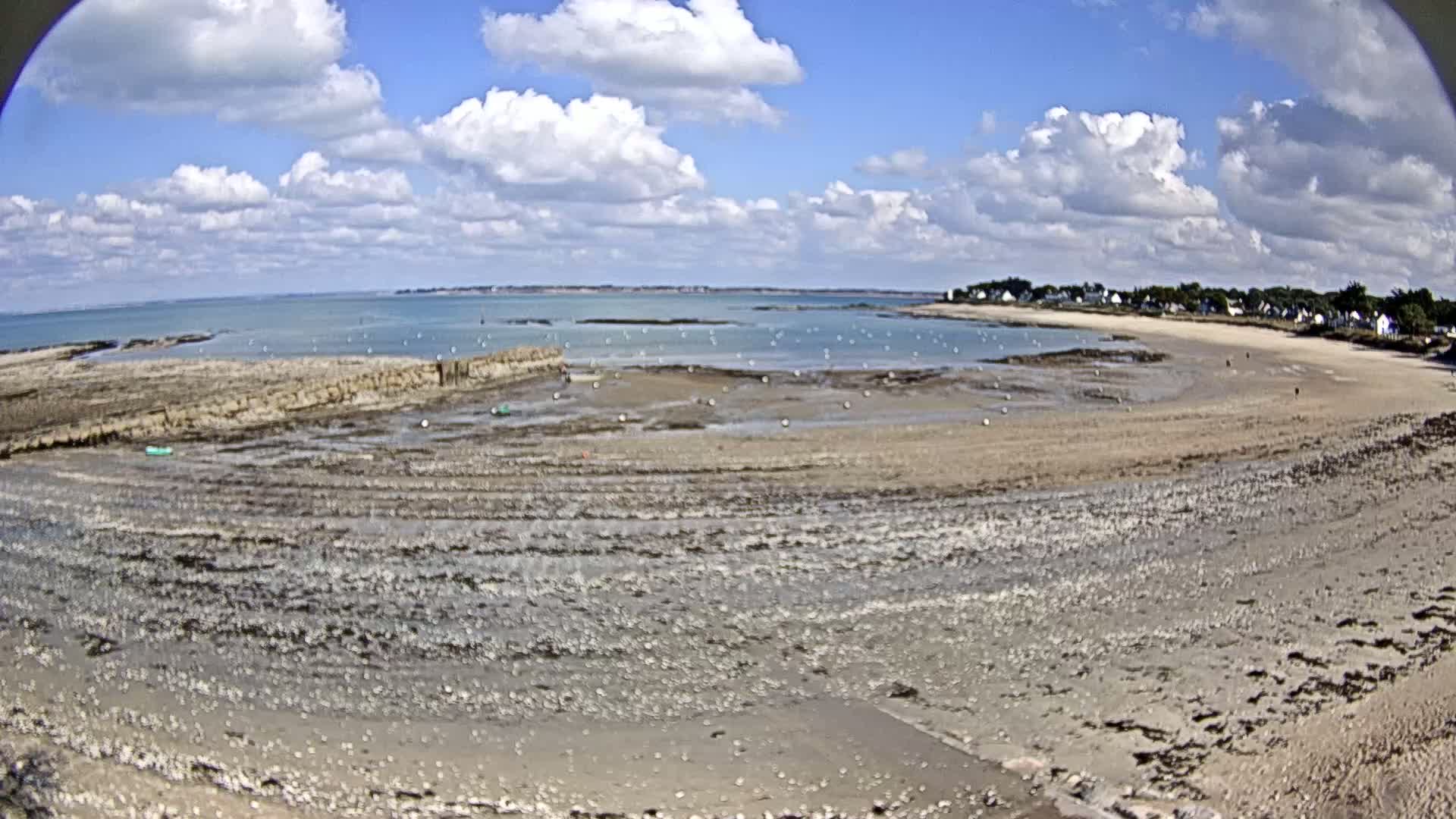A wide, sandy beach at low tide stretches towards a calm ocean under a partly cloudy sky.