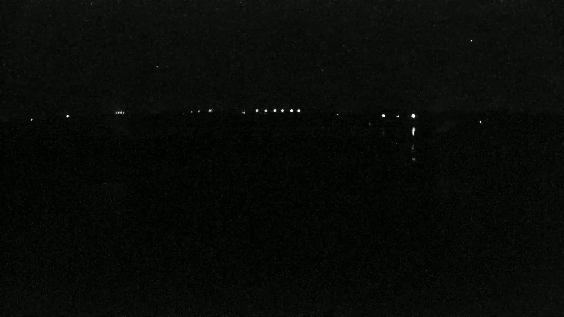 A dark, nighttime scene shows a line of distant lights on the horizon under a clear, starry sky.