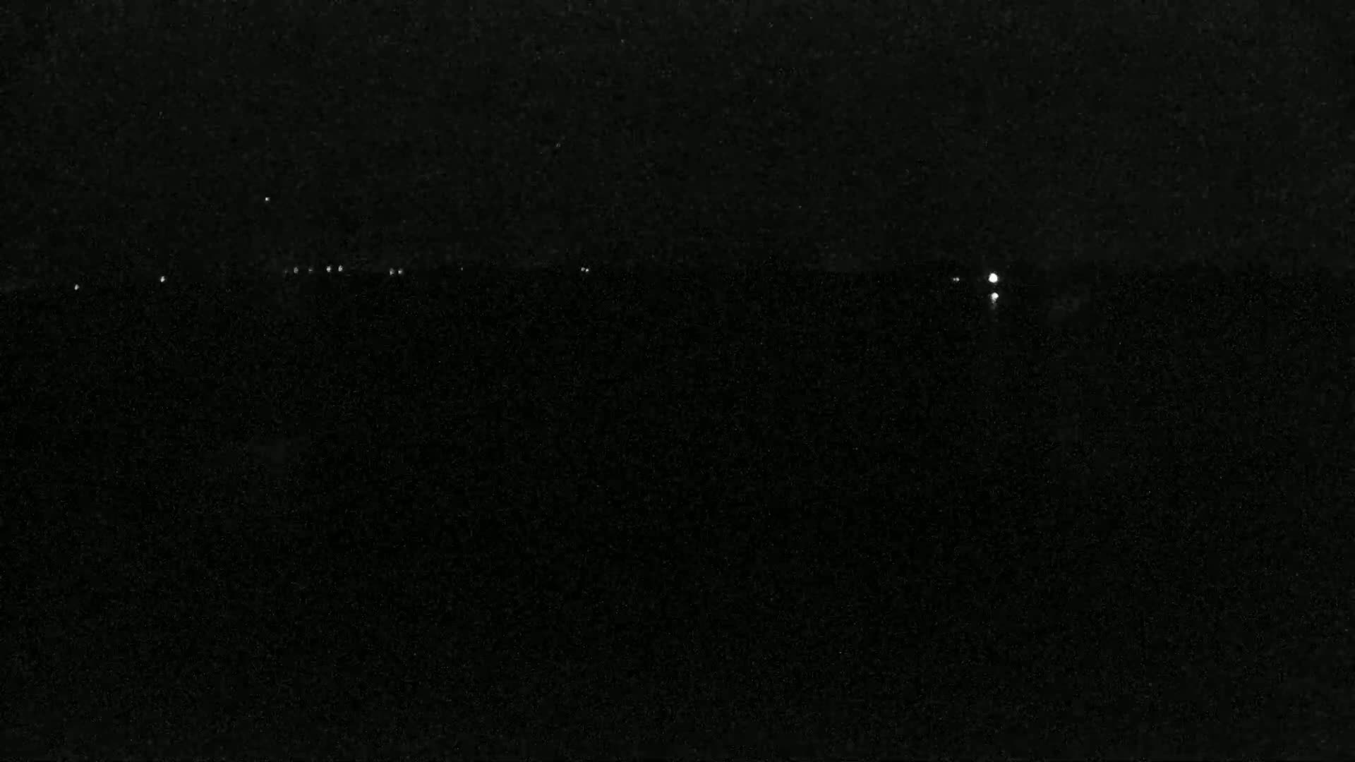 A nighttime view of a dark landscape with a few distant lights on the horizon.