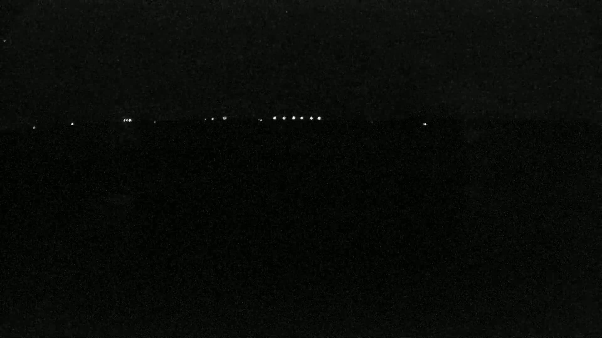 A nighttime image shows a line of faint lights on a dark horizon.