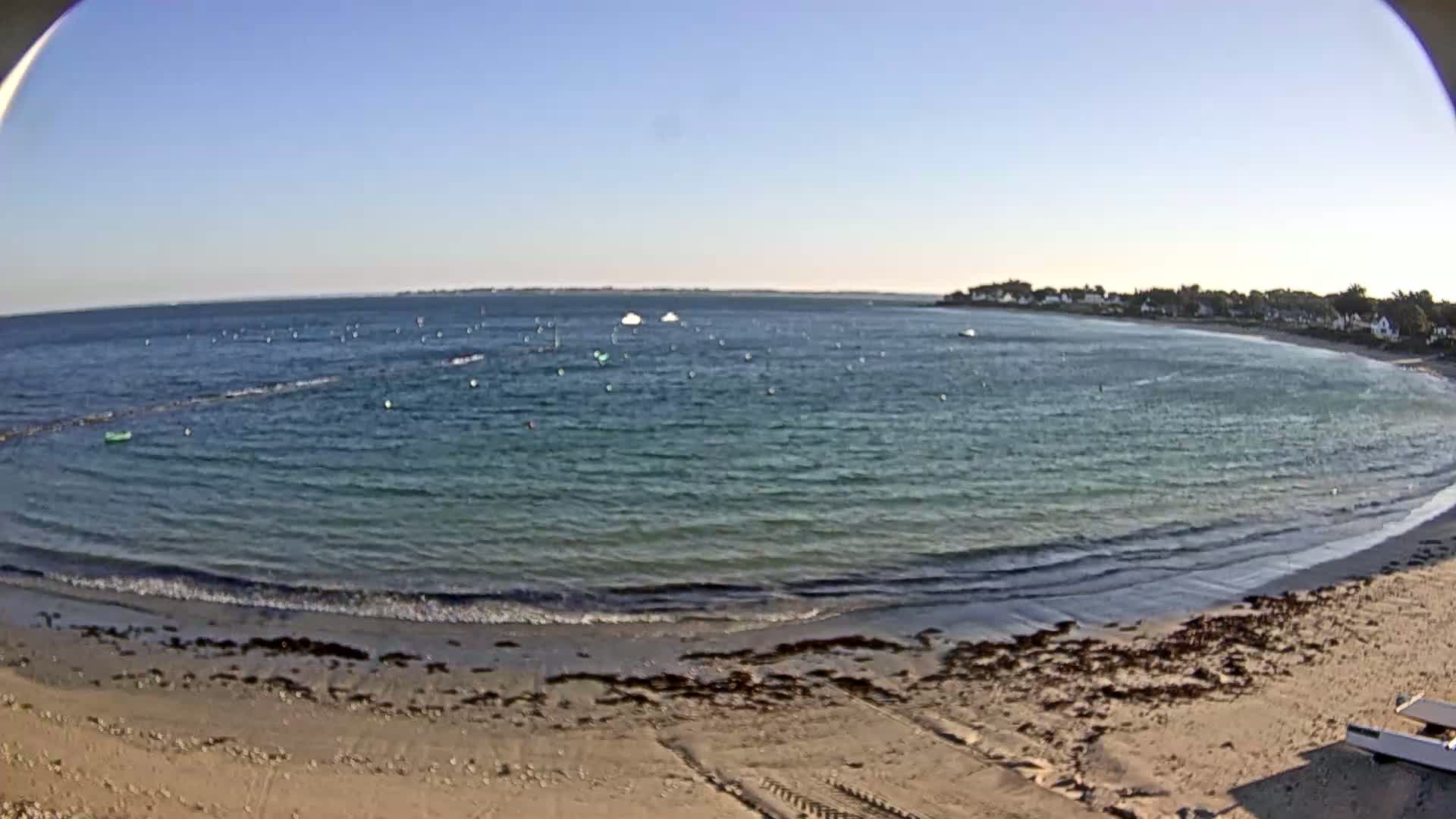 A sandy beach curves gently into a calm, teal ocean under a clear blue sky.