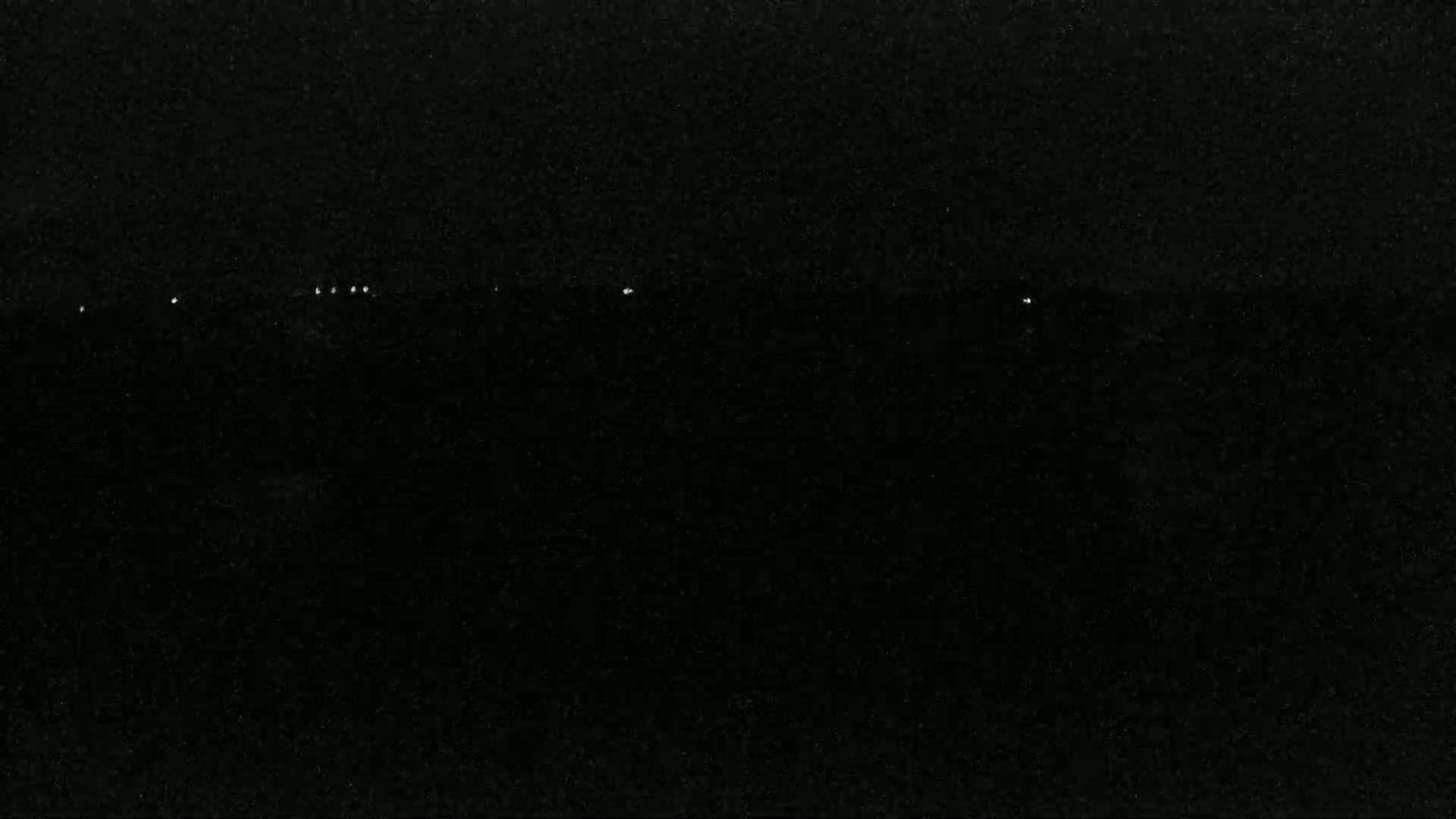 A dark, nighttime scene shows a horizontal line of faint, distant lights against a mostly black sky.