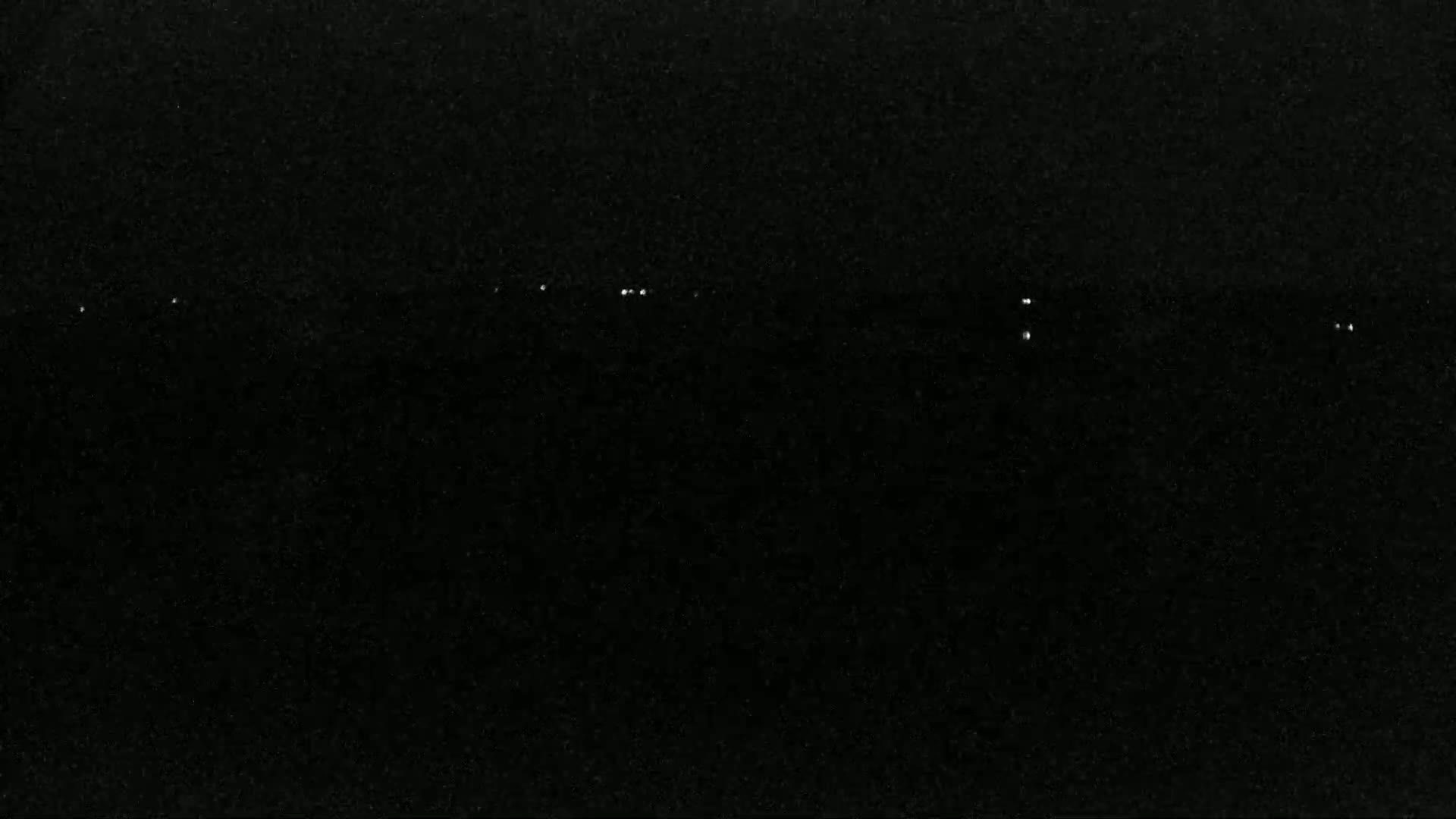A dark, nighttime scene shows a few faint, distant lights on a dark horizon.