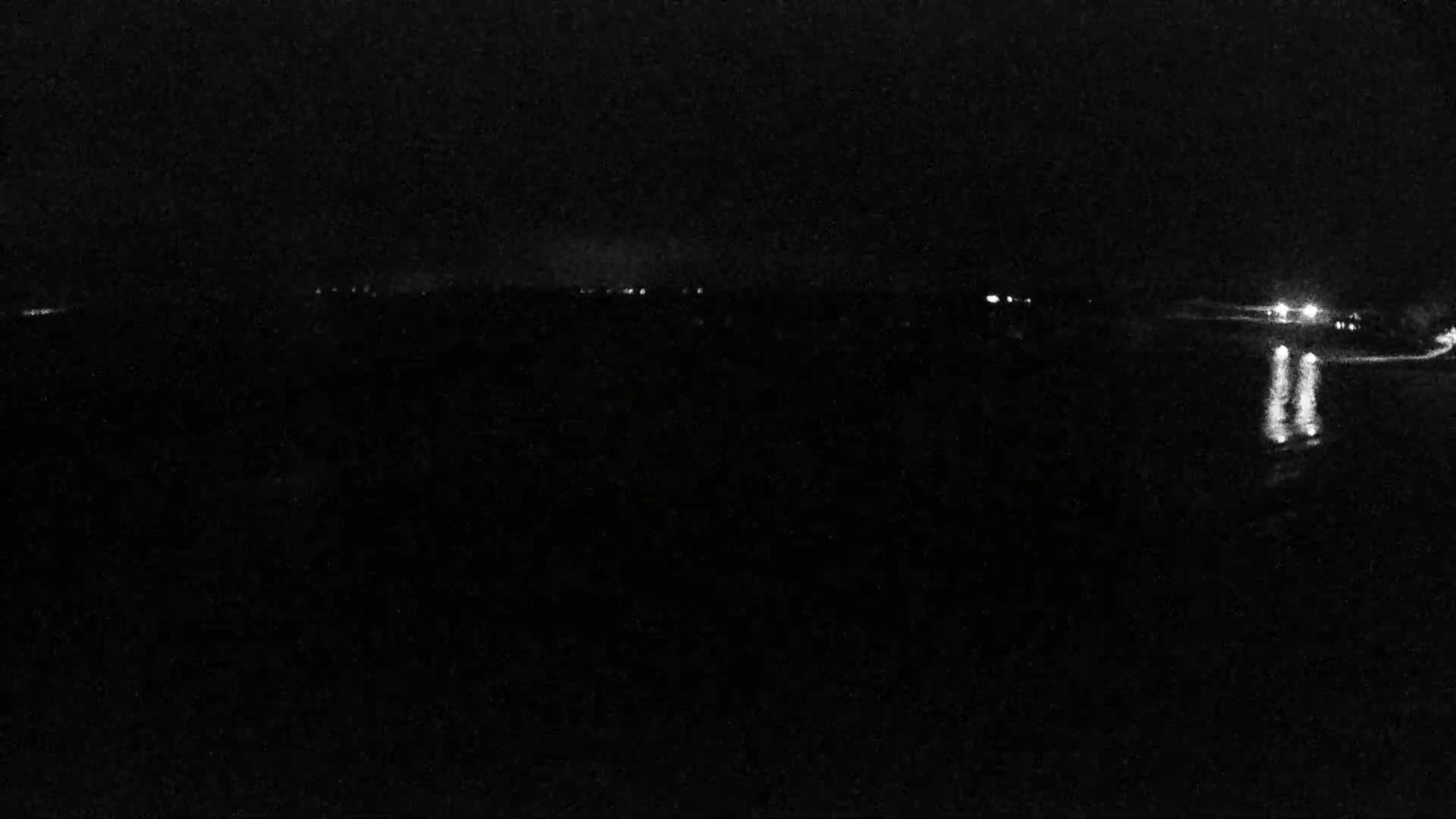 At night, a dark body of water reflects the faint lights of a distant shoreline.