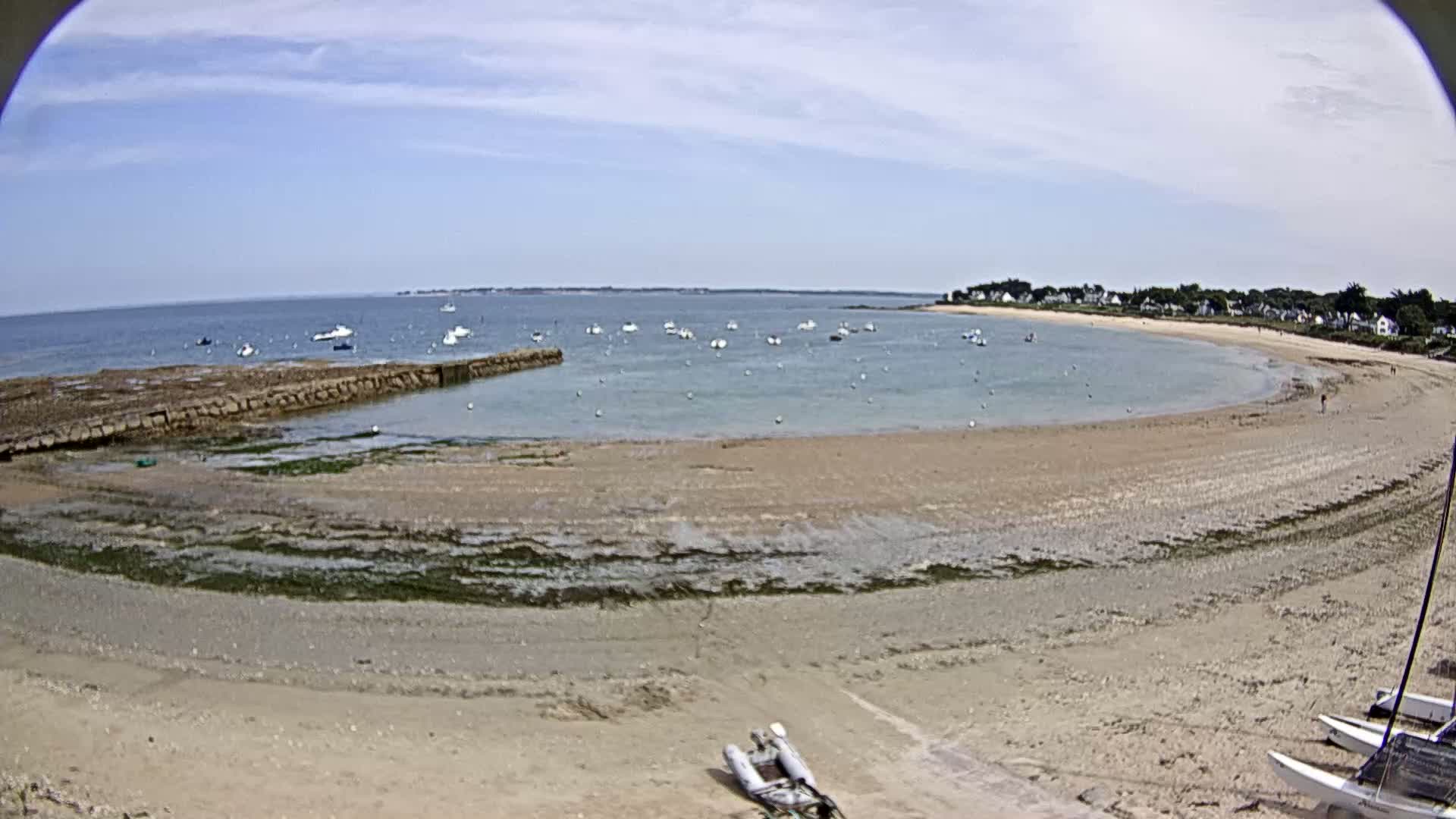 A sandy cove with numerous small boats in calm water under a partly cloudy sky.